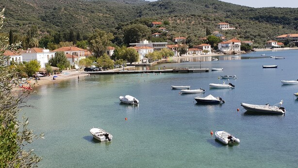 A coastal town with boats docked along the shore, surrounded by hills and residential buildings. - Zmas Studios (South Pelion)