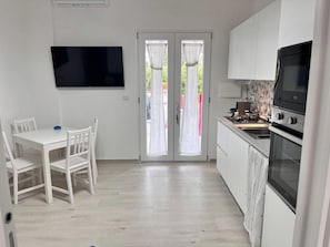 A modern kitchen with white cabinetry, a built-in oven, and a dining area with a white table and chairs.