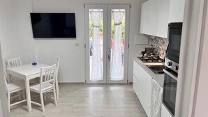 A modern kitchen with white cabinets, a built-in oven, and a dining area with a white table and chairs. - Formia Seaside Apartment With Beautiful Terrace (Formia)