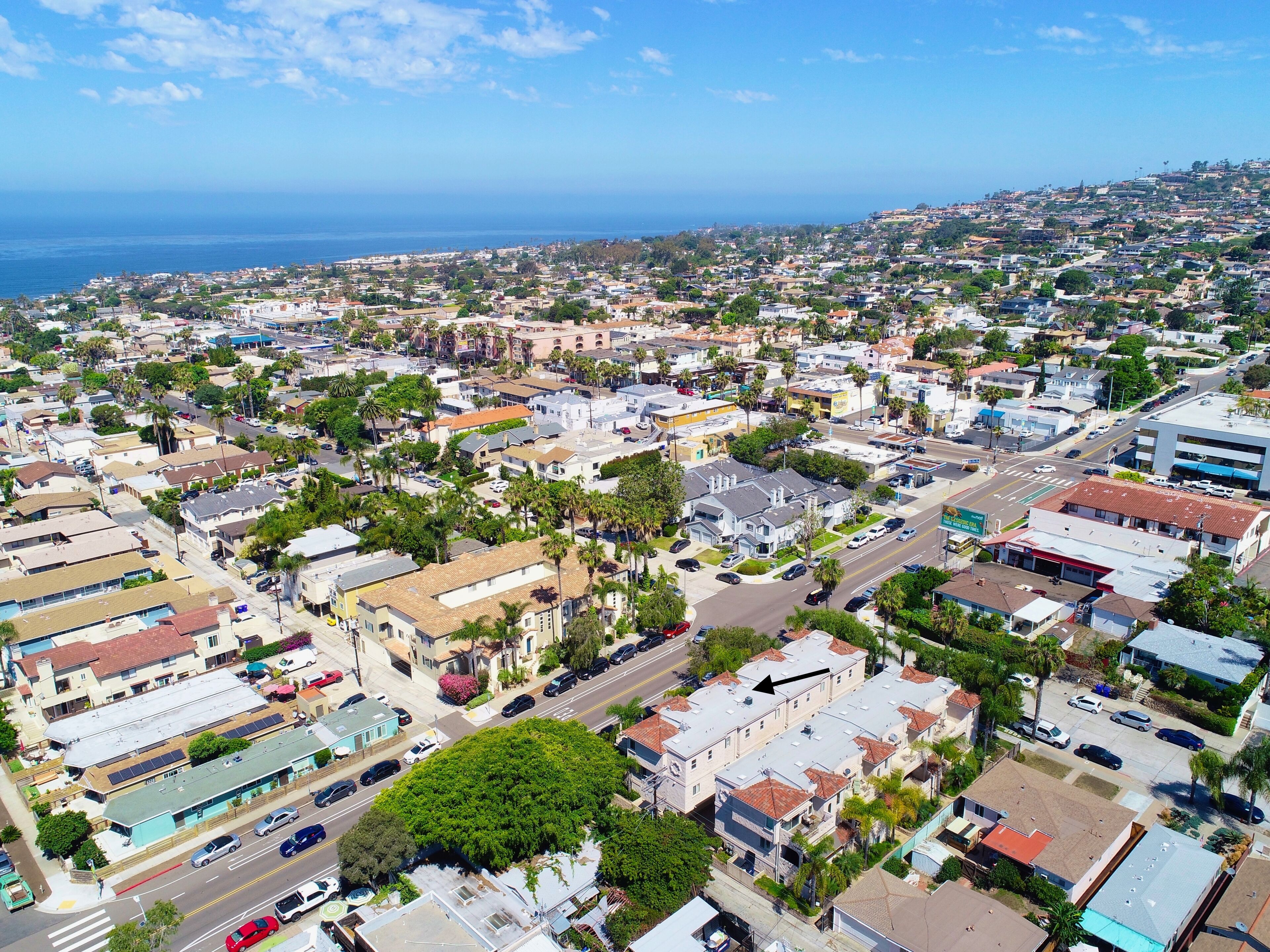 An aerial view of a coastal town with a mix of residential and commercial buildings, roads, and visible greenery.