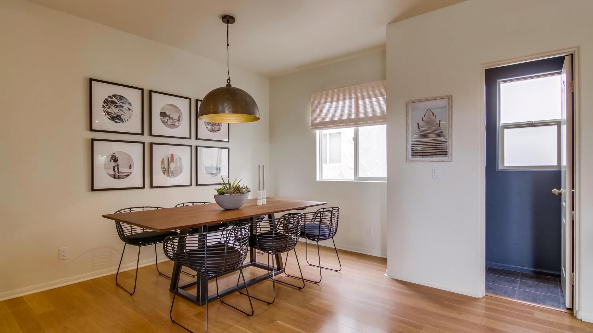 A dining area with a wooden table, black wire chairs, and a hanging pendant light.