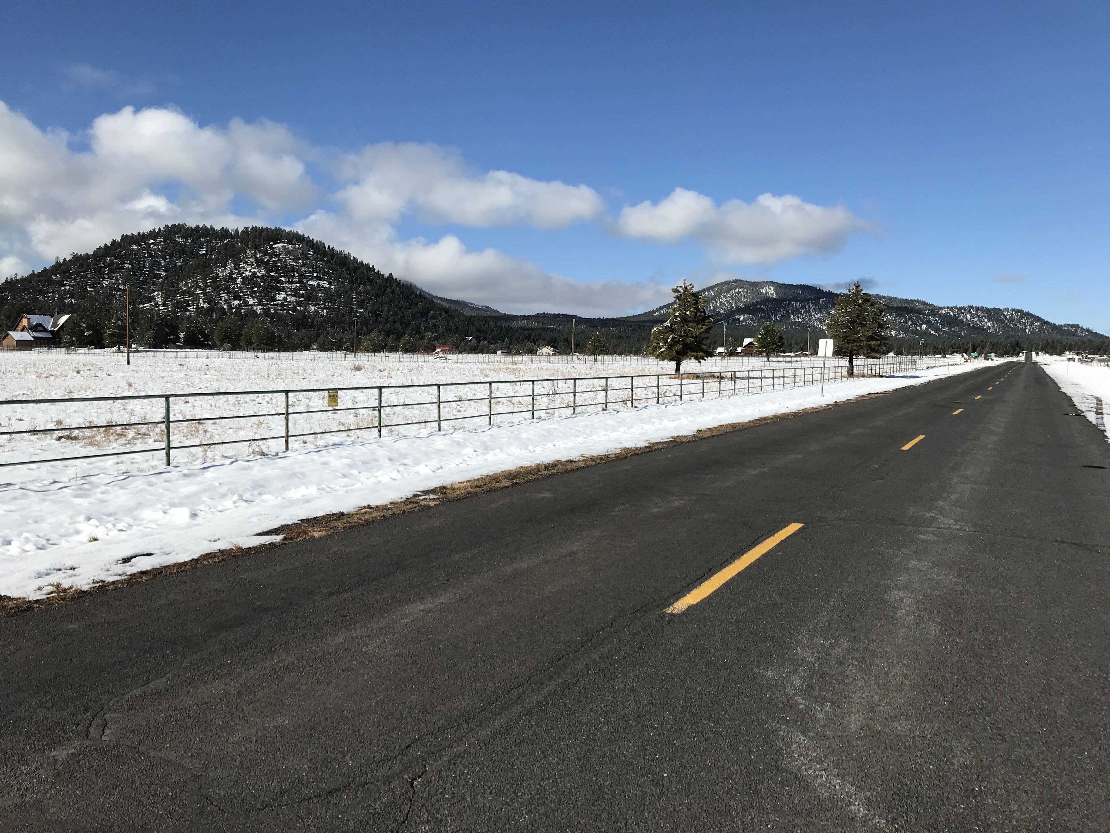 Une route enneigée, bordée d’une clôture métallique d’un côté et avec une montagne en arrière-plan.