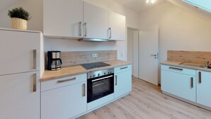 A modern kitchen with white cabinetry, a built-in oven, and a coffee maker. - Apartment in historical building - old school (Spittelstein)
