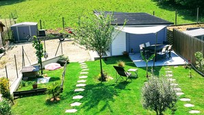 Un jardin à l’arrière d’une maison, avec une terrasse, un espace salon extérieur et un petit abri de jardin.