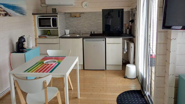 Une cuisine compacte équipée d’un four à micro-ondes, d’un évier et d’un lave-vaisselle, un coin repas avec une table et des chaises, et une grande fenêtre avec des rideaux.