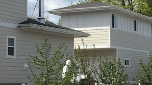 Un bâtiment à deux étages avec une cheminée, un espace clos entouré d’arbres et un ciel dégagé.