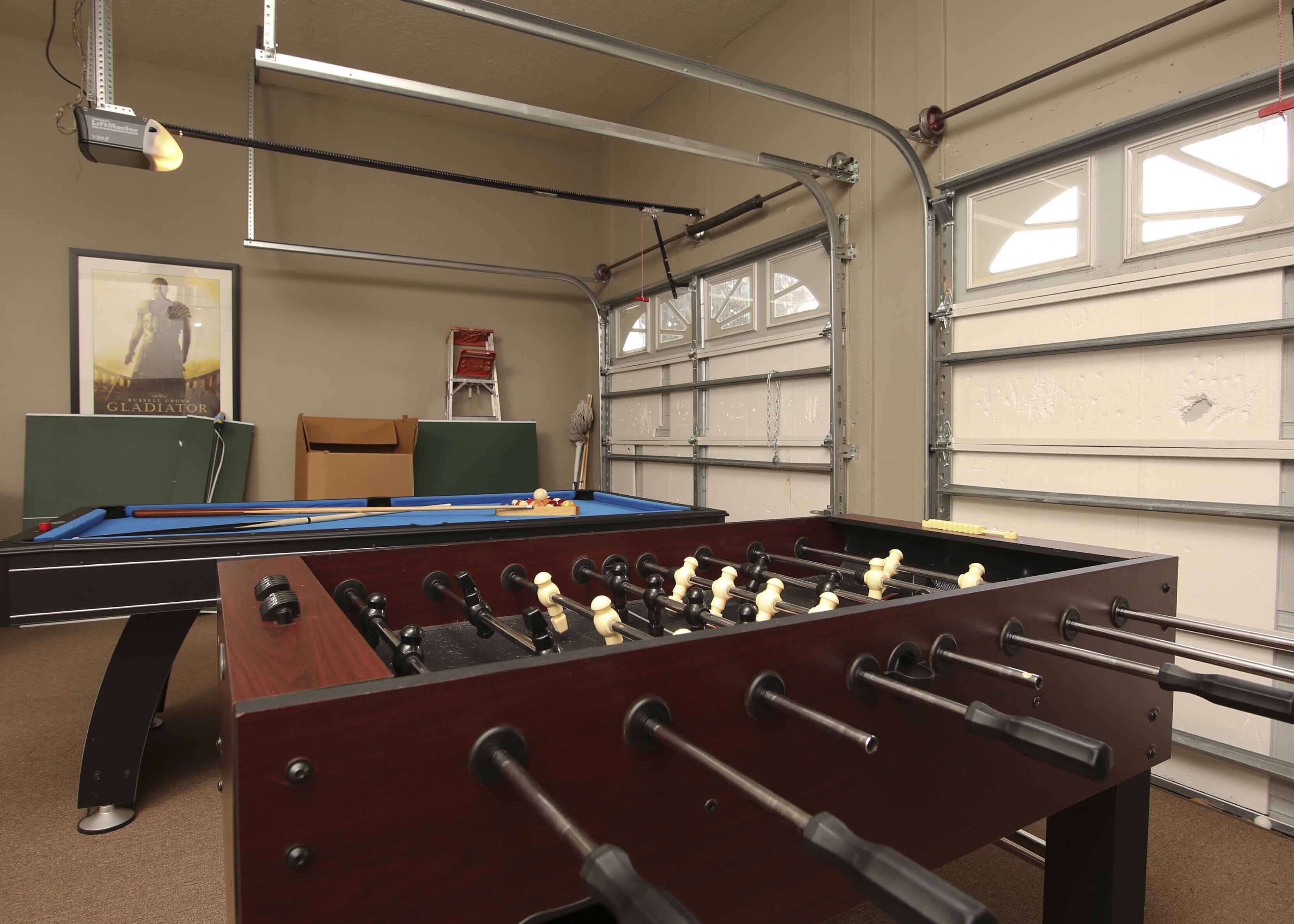 A pool table with a foosball table in front, a green chair, and a framed movie poster on the wall.