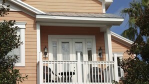 Uma casa com varanda, corrimãos brancos e duas janelas com persianas brancas.