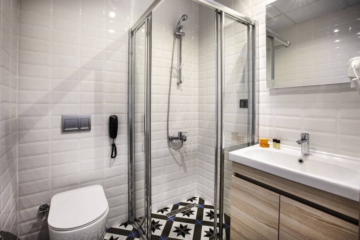 Un baño moderno con ducha de vidrio, inodoro blanco, lavamanos con artículos de aseo y un espejo.