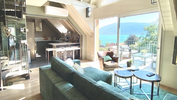 Een ruime woonkamer met een grote bank, een eettafel en uitzicht op zee.