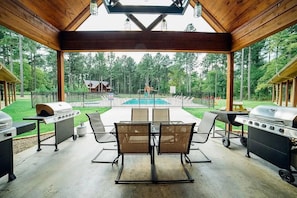 Relax in the serene outdoor patio area, complete with a barbecue grill and dining table, overlooking the pool and surrounded by trees.