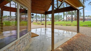 A covered outdoor area with a concrete floor, wooden beams, and a stone wall.