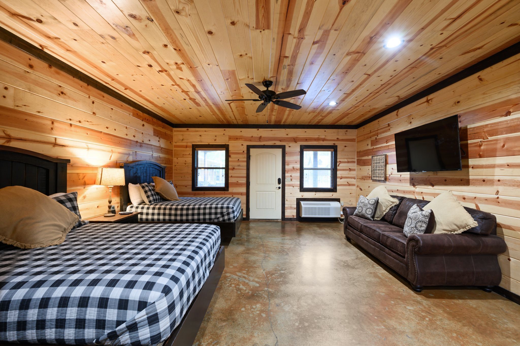A cabin interior with two beds, a sofa, a ceiling fan, a TV, and a door.