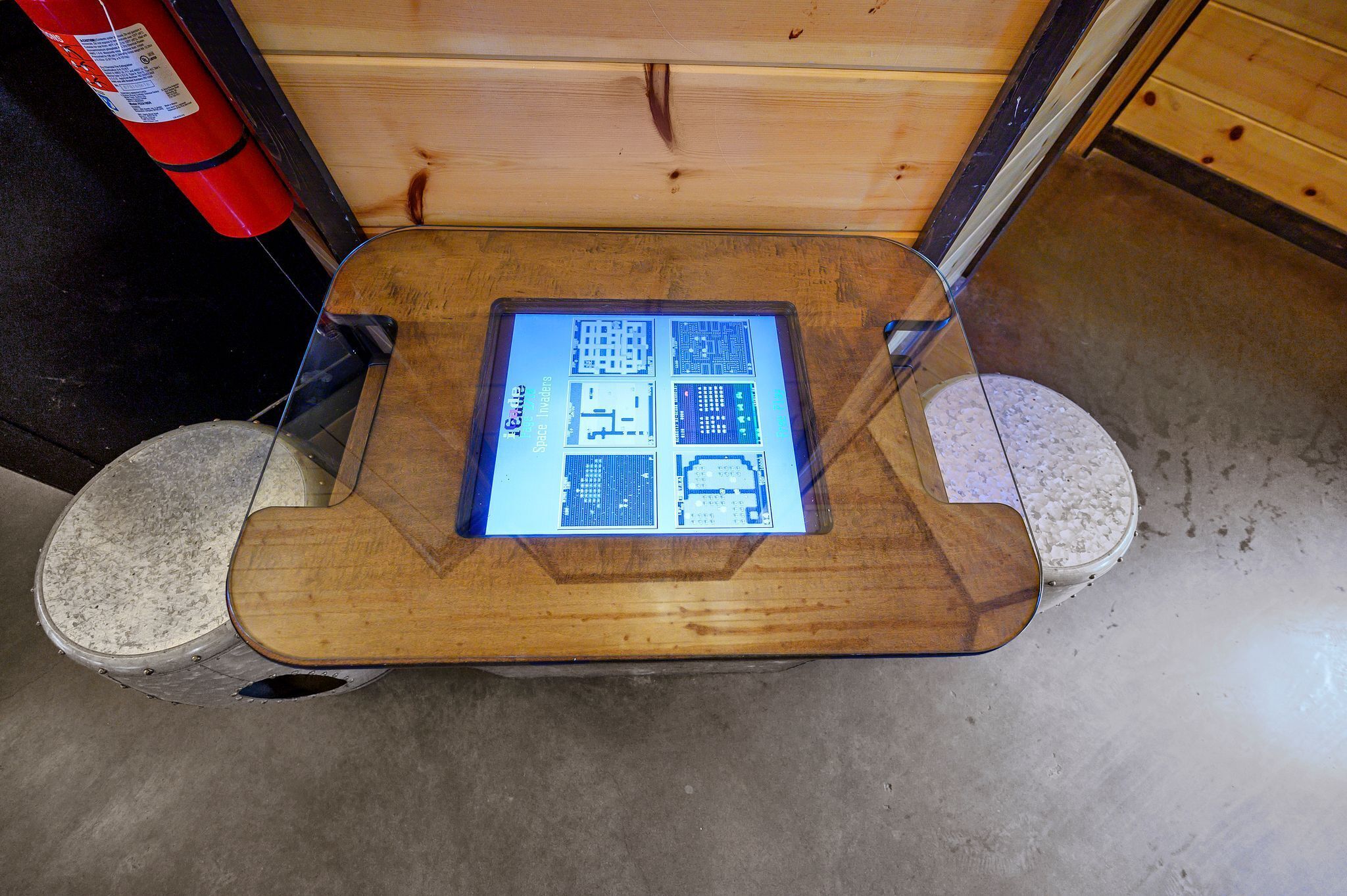 Una mesa de madera con una pantalla digital en el centro, rodeada por un suelo de concreto y una pared de madera.