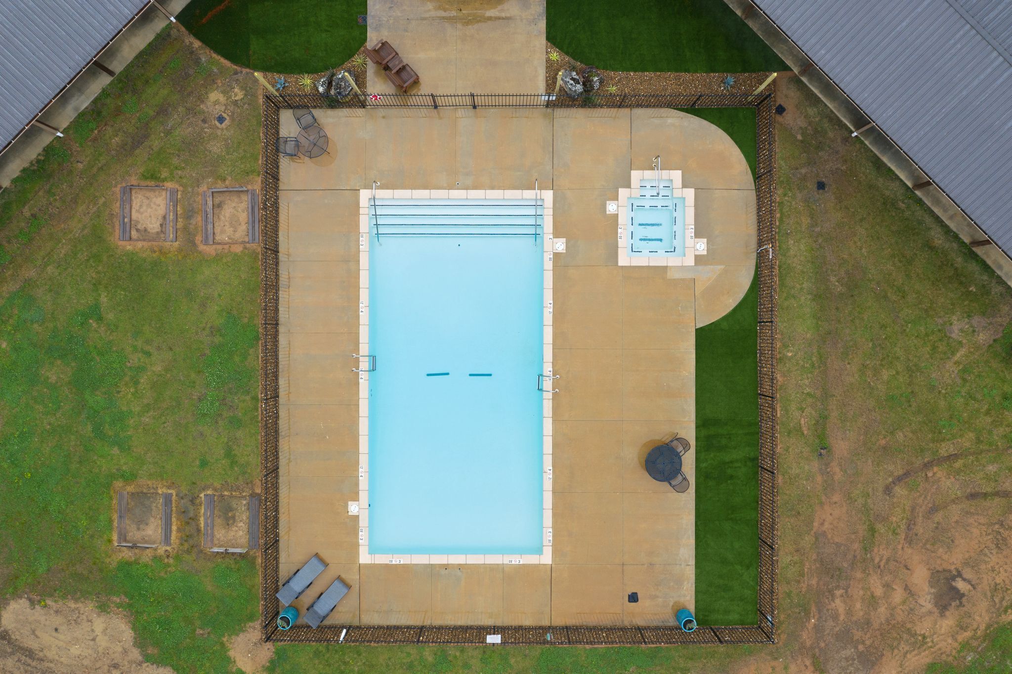 Vue aérienne d’un espace piscine comprenant une piscine rectangulaire, un plongeoir et une petite terrasse avec des sièges.