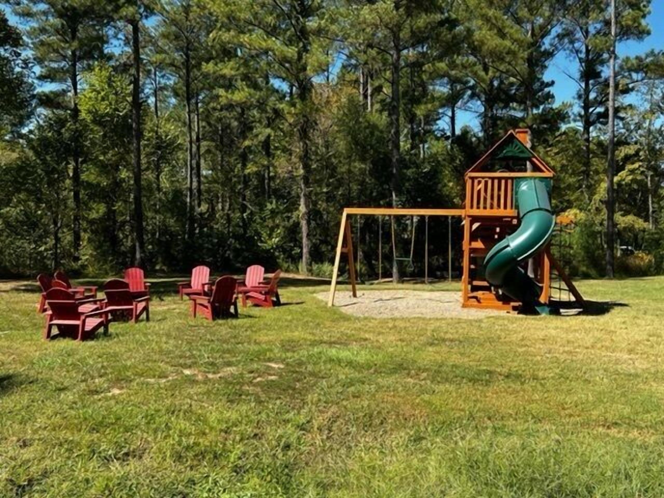 A playground with a slide and swings, surrounded by trees.