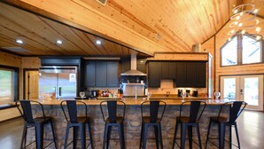 A modern kitchen with a stone island, black bar stools, and wooden ceiling.