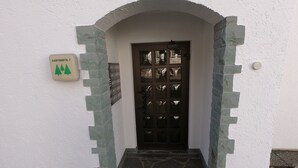 Ein weißes Gebäude mit einem steinernen Bogen, der zu einer dunklen Holztür führt. Auf der linken Seite ist ein Schild mit grünen Bäumen und dem Text 