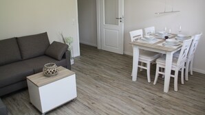 Ein modernes Wohnzimmer mit grauem Sofa, einem weißen Couchtisch und einem Essbereich mit einem Holztisch, gedeckt für vier Personen.