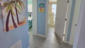 Un couloir aux murs bleu clair, doté d’un plancher en bois et d’une porte donnant sur une autre pièce.