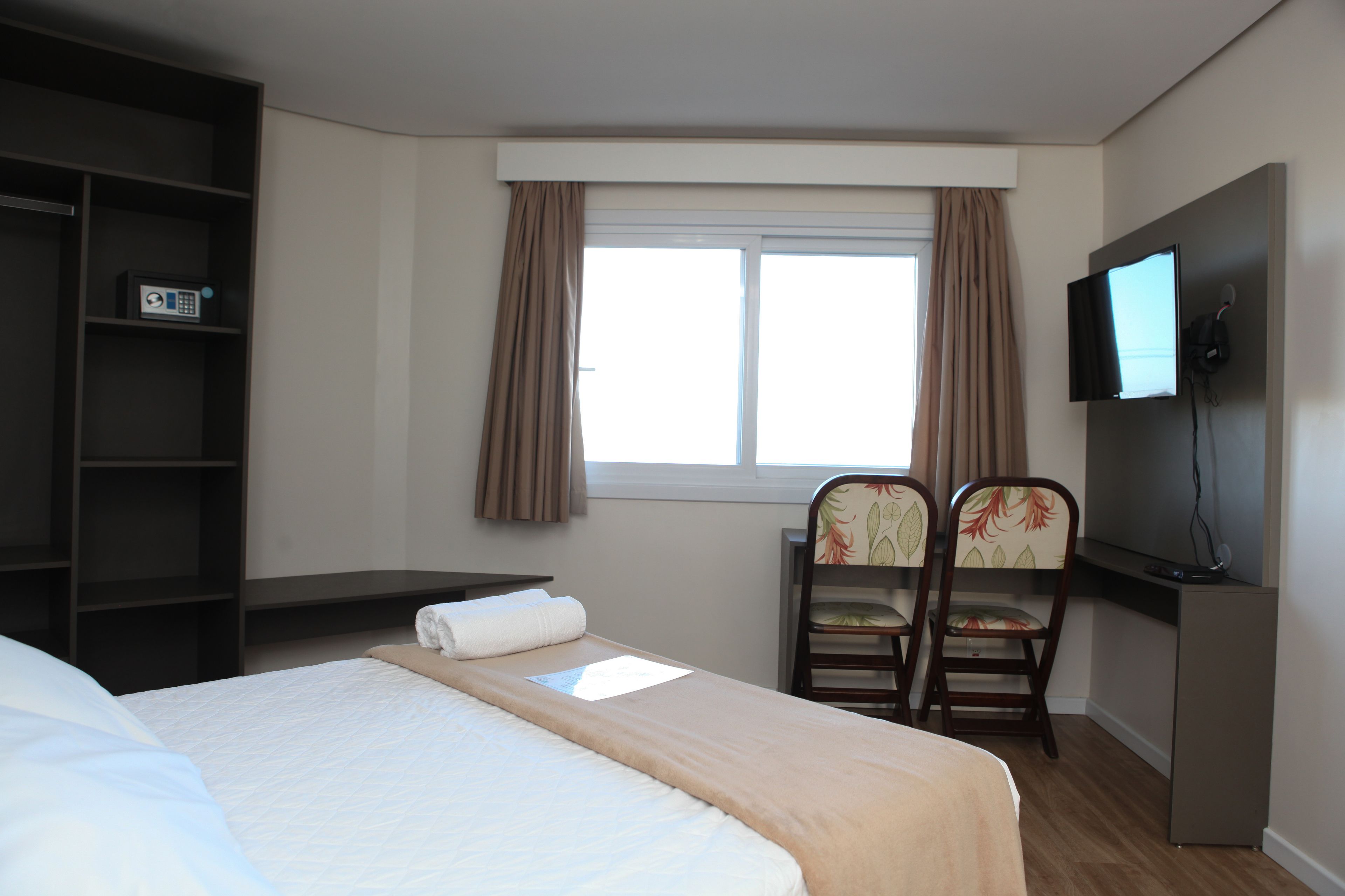 Una habitación de hotel con una cama, un escritorio con silla, televisión y ventana con cortinas.