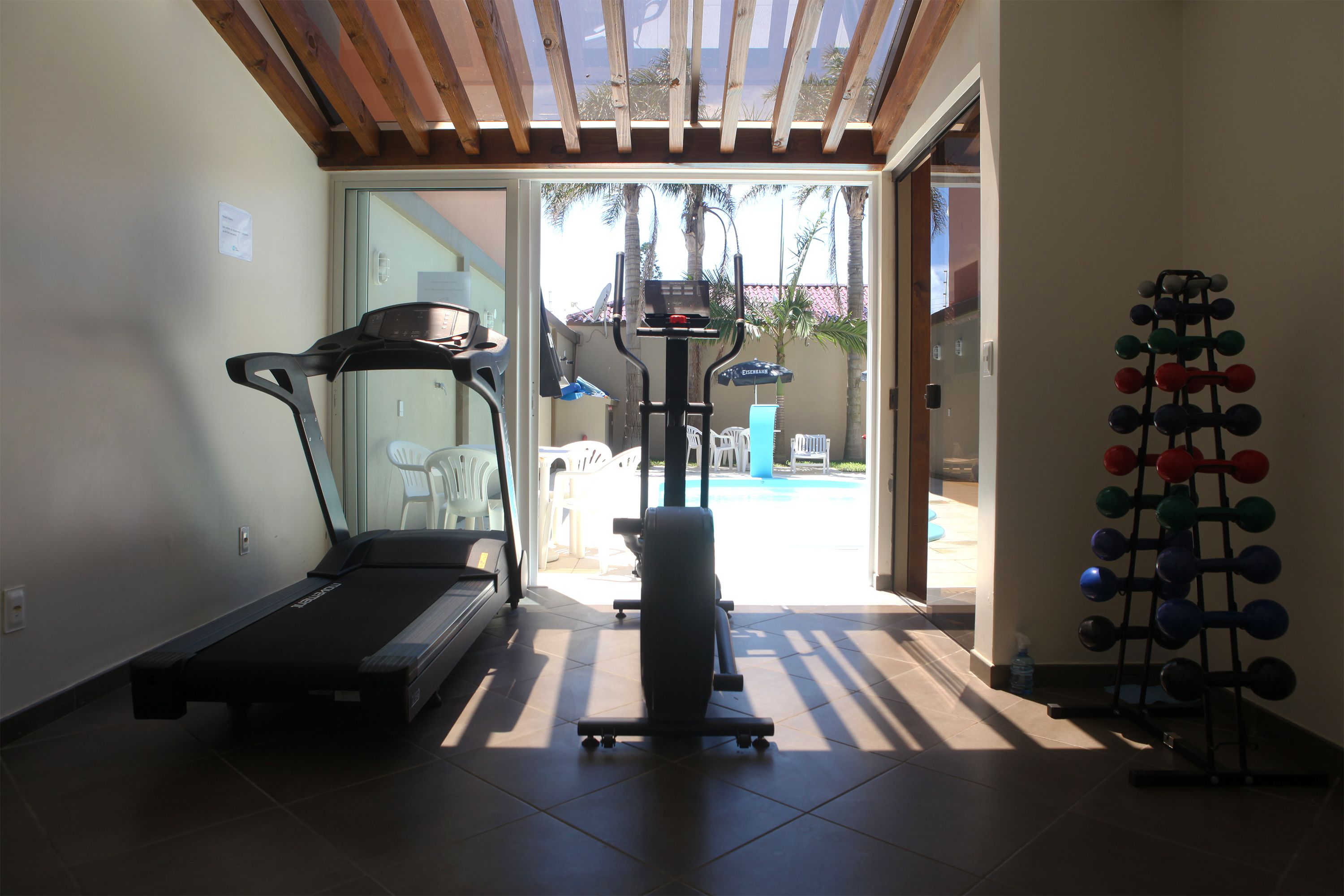 Een fitnessruimte thuis met een loopband, elliptische trainer en een rek voor gewichten.