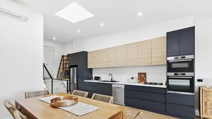A modern kitchen with dark cabinetry, a wooden dining table, and a built-in oven. - Point Break (Anglesea)