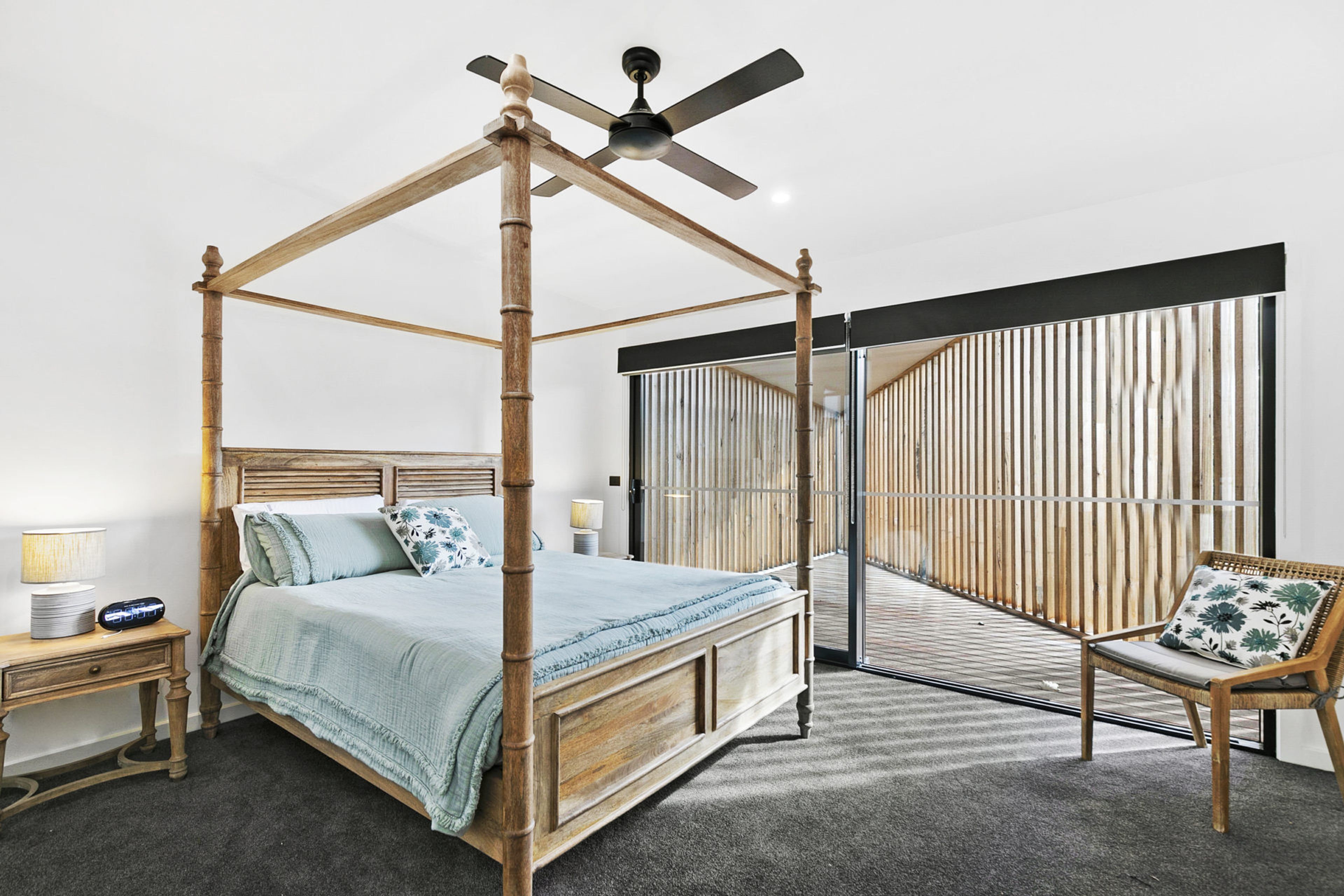 Een hemelbed met houten hoofdbord, een nachtkastje met lamp en een fauteuil met kussen.