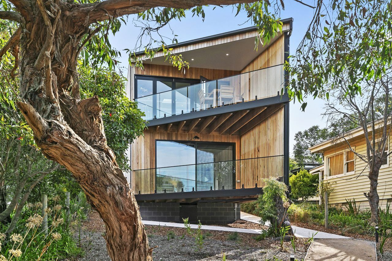 A modern two-story house with a balcony, large windows, and a wooden exterior.