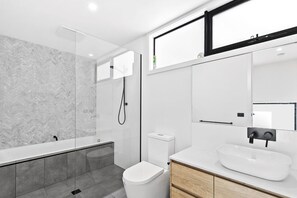 A modern bathroom with a glass-enclosed shower, a white toilet, and a sink with a mirror above.