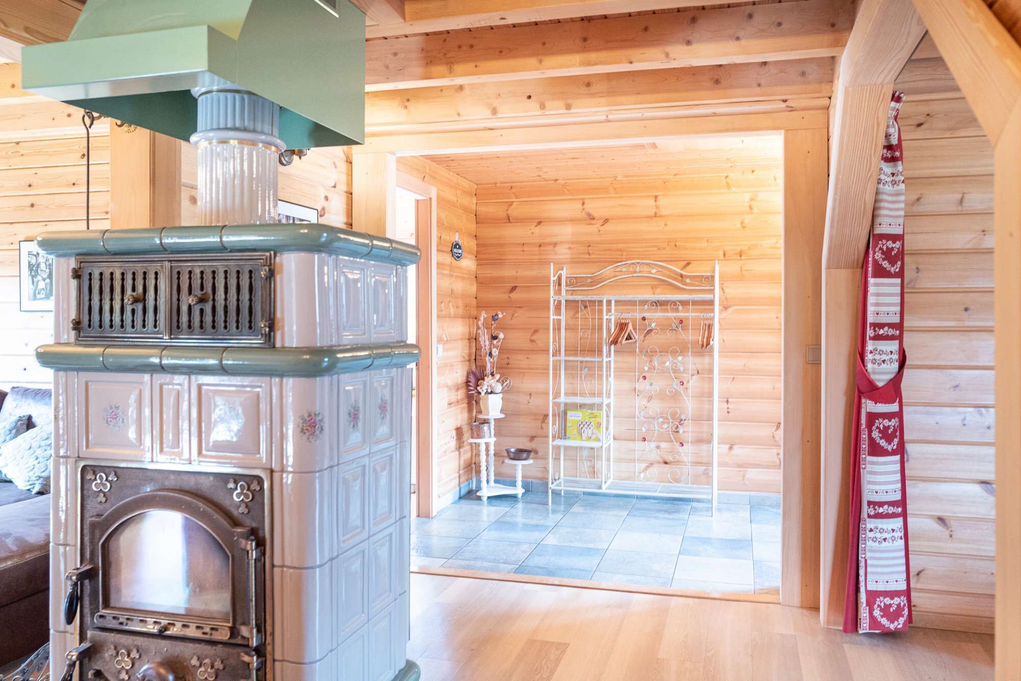 A wooden cabin interior with a vintage stove, a metal rack with items, and a red decorative cloth.