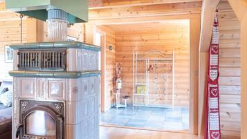 A wooden cabin interior with a vintage stove, a metal rack with items, and a red decorative cloth.
