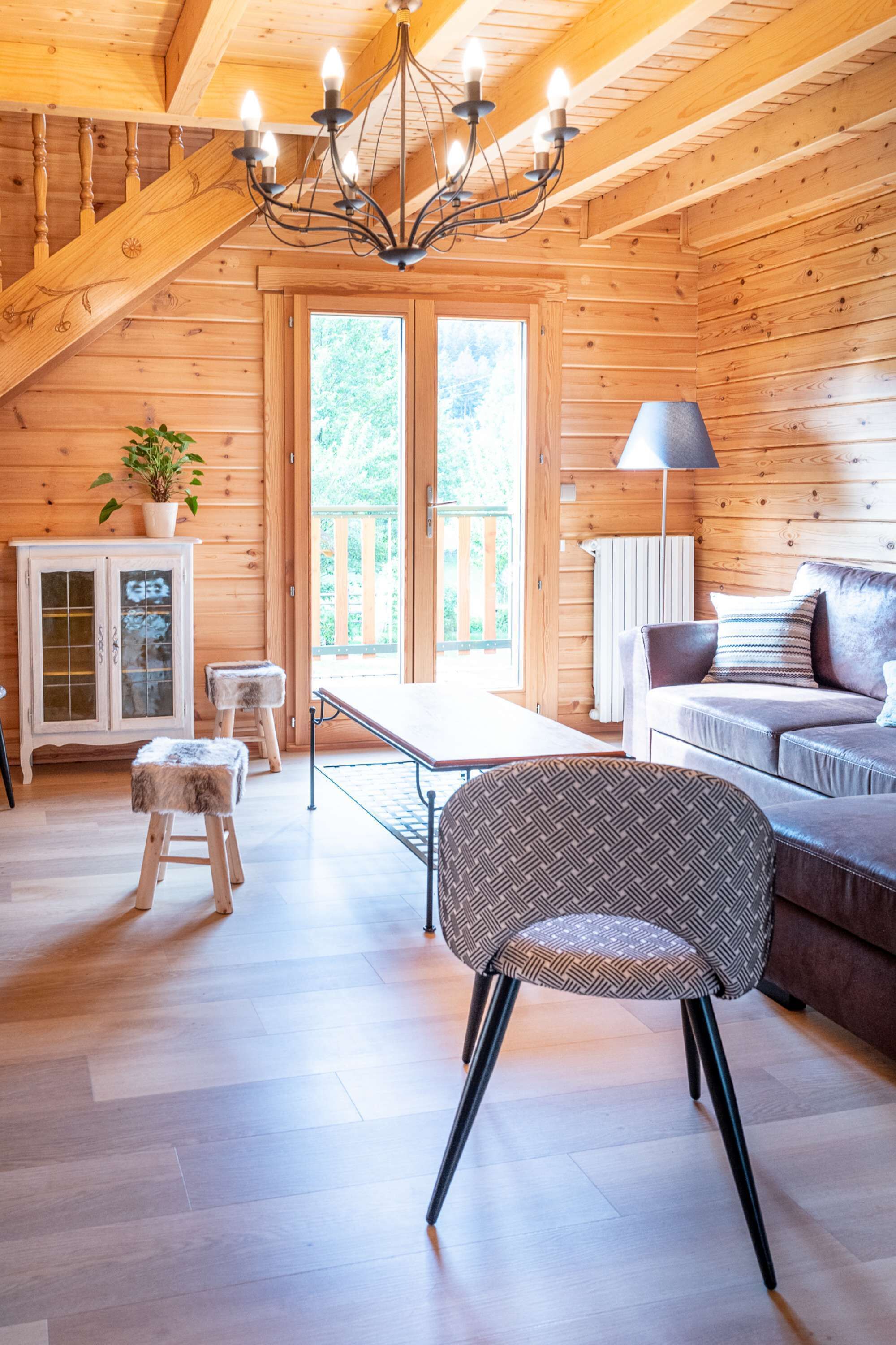 A wooden cabin interior with a dining table, sofa, and a chandelier.