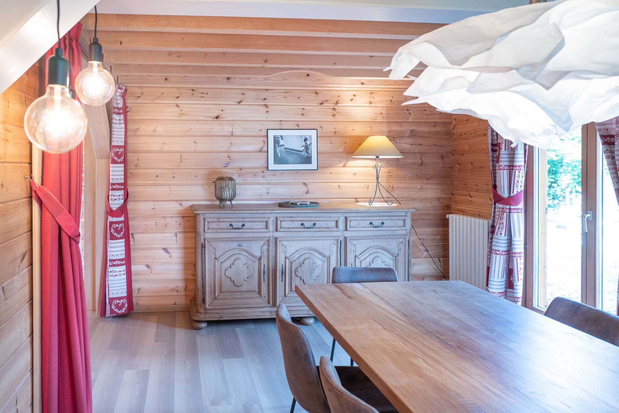Een houten interieur met een eettafel, stoelen, een kast en een lamp.