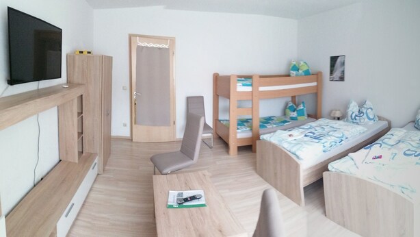 Una habitación con una cama litera, un escritorio con silla, un televisor montado en la pared y una puerta con cortina.