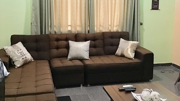 A living room with a sectional sofa, a coffee table, and a wall-mounted air conditioner. - Gees Shortlets Apartments (Lagos)