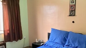 A bedroom with a large bed, a nightstand, a wall-mounted light, and a window with curtains. - Gees Shortlets Apartments (Lagos)