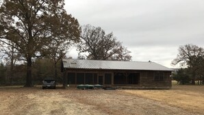 A rustic cabin with a metal roof, surrounded by trees and a gravel driveway. - Cabin in the woods between Mt. Nebo and Mt. Magazine (Dardanelle)