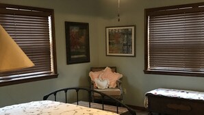 A bedroom with a bed, a chair, a small table, and two windows with blinds. - Cabin in the woods between Mt. Nebo and Mt. Magazine (Dardanelle)
