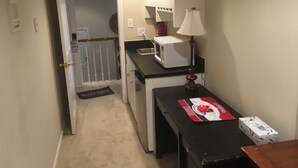 A compact kitchen with a microwave, a table with a placemat, and a lamp. A door leads to a staircase. - Professional, Travelers Haven , 1 bdrm, living room, private shower free parking (Martinez)