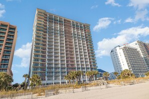 A high-rise hotel with multiple balconies, located near a beach with a sandy foreground and palm trees. - Amazing Oceanfront 2 Bed 2 Bath Condo in Myrtle Beach (Myrtle Beach)