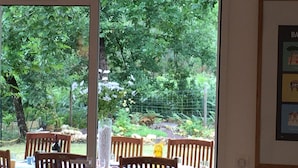 Ein Essbereich mit Holztischen und -stühlen, eine Glastür zu einem Garten mit Bäumen und einem Zaun.