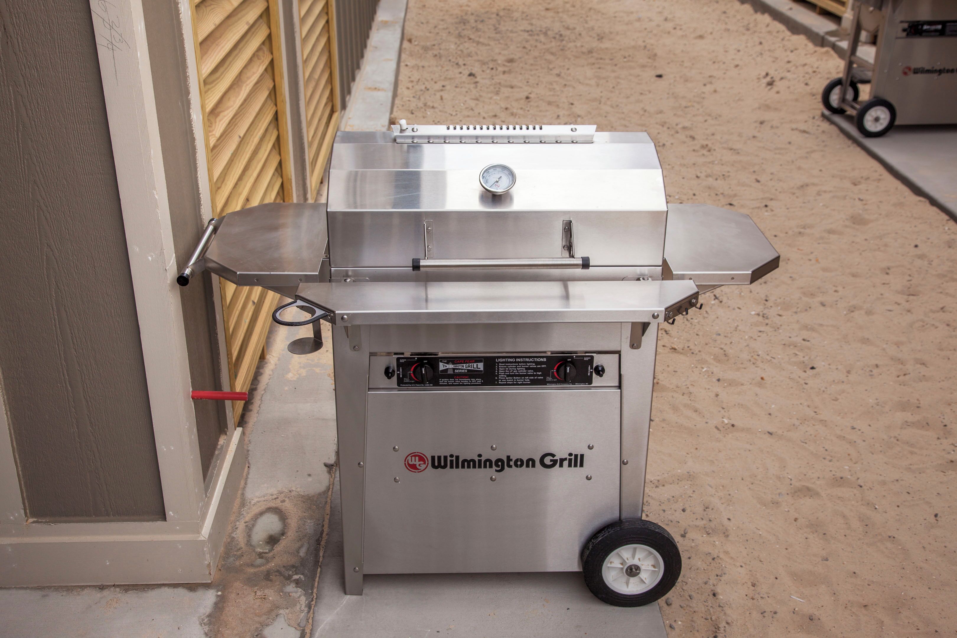 A portable grill with wheels, branded 'Wilmington Grill', placed on a concrete surface near a building.