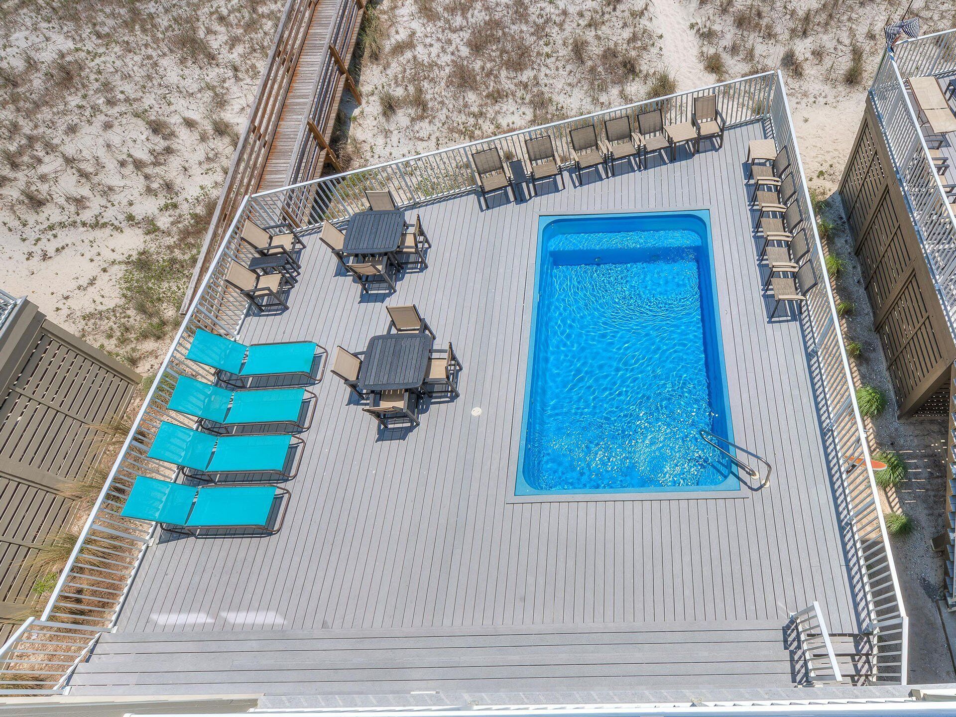 An aerial view of a rooftop pool area with a rectangular pool, multiple lounge chairs, and a wooden deck.