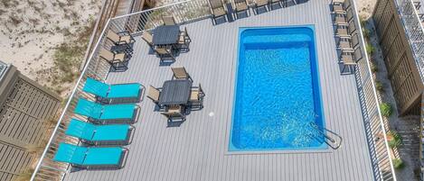 An aerial view of a rooftop pool area with a rectangular pool, multiple lounge chairs, and a wooden deck.