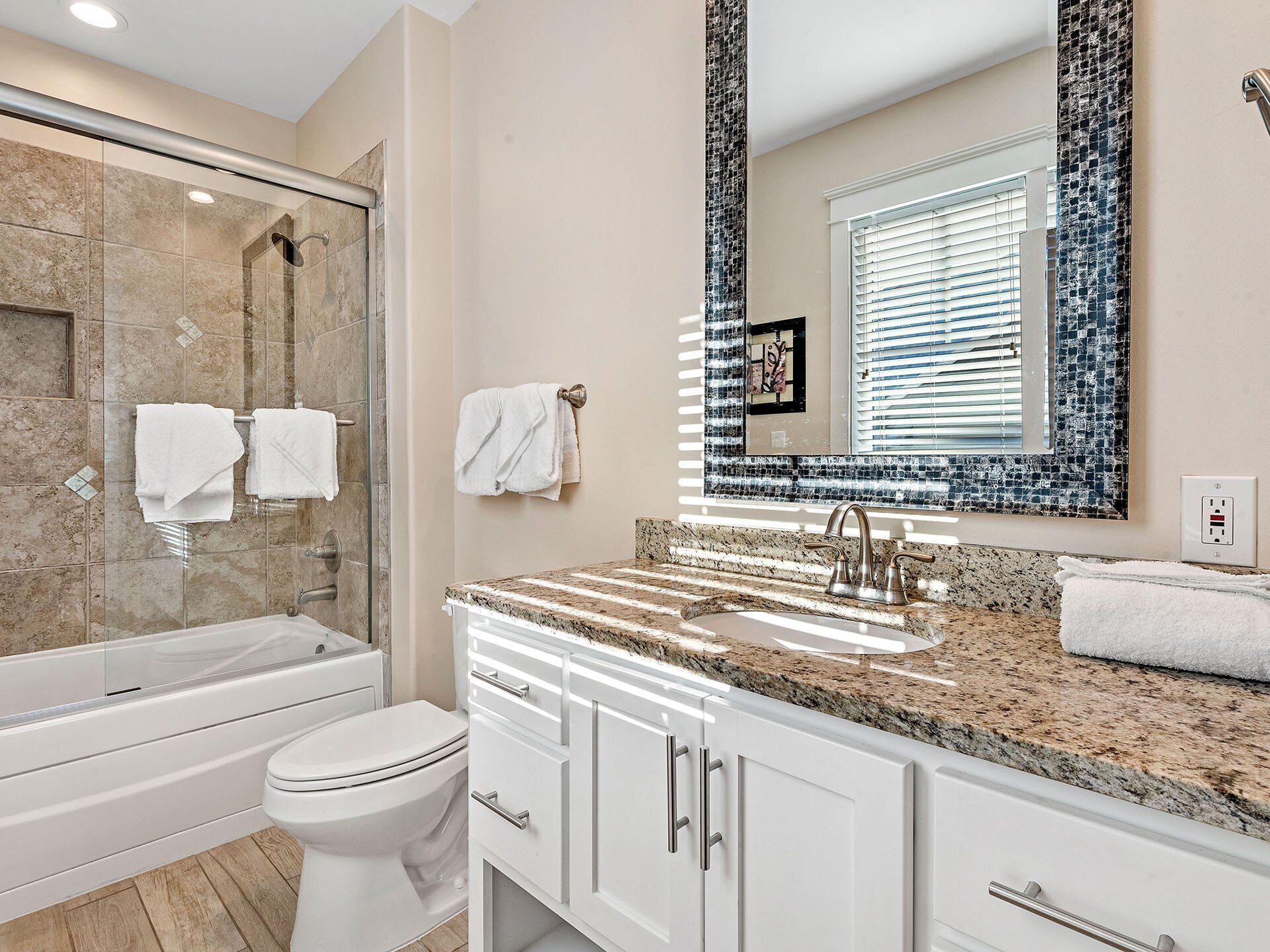 Une salle de bain moderne avec une douche à parois de verre, des toilettes blanches, un lavabo sur un plan de travail en granit et des meubles blancs.