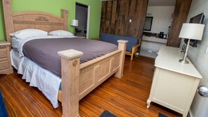 A bedroom with a wooden bed, a nightstand, a bedside table, a chair, a desk, and a mirror. - Camrose Motel (Camrose)