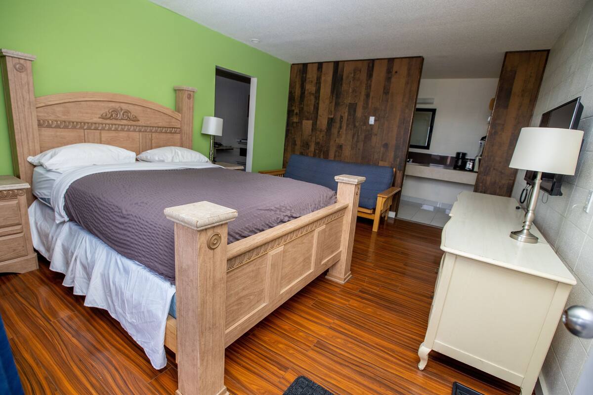 A bedroom with a wooden bed, a nightstand, a bedside table, a chair, a desk, and a mirror.