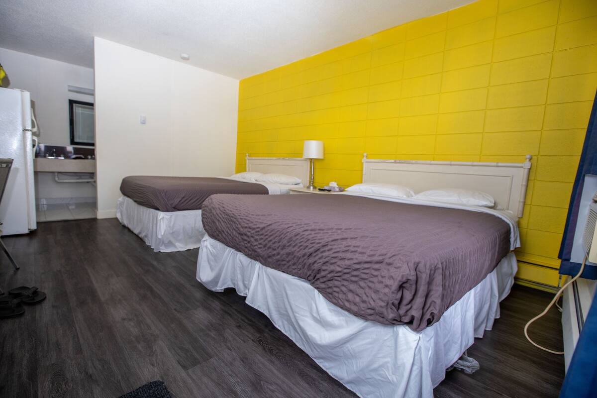 A hotel room with two beds, a kitchenette, and a bright yellow accent wall.