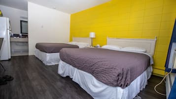 A hotel room with two beds, a kitchenette, and a bright yellow accent wall.